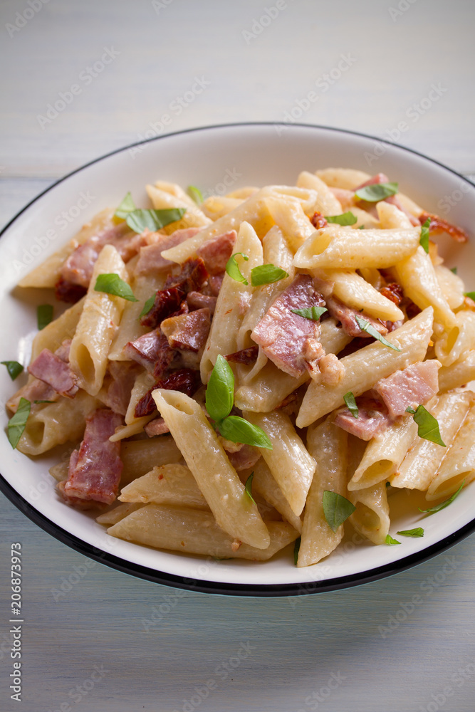 Penne pasta with bacon and sundried tomatoes. Alfredo penne pasta on white plate on wooden table. vertical Penne pasta with bacon and sundried tomatoes. Alfredo penne pasta on white plate on wooden table. vertical