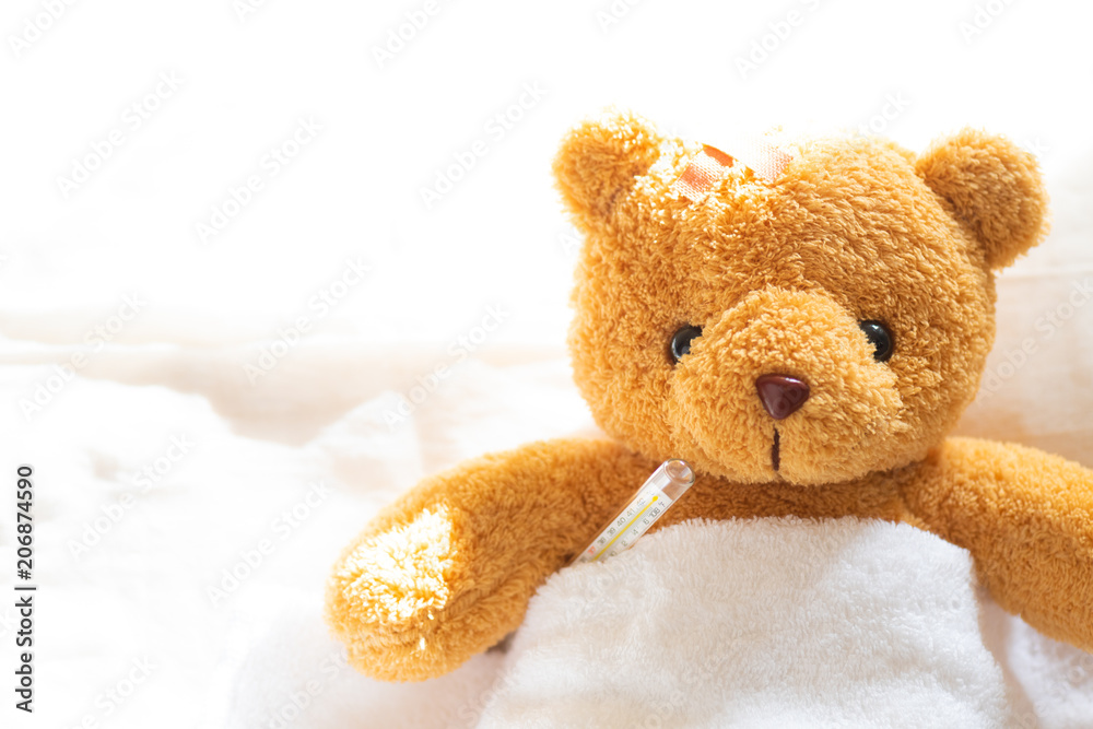 Teddy bear lyiing sick in hospital bed with with thermometer and plaster. Healthcare and medical concept.