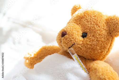 Teddy bear lyiing sick in hospital bed with with thermometer and plaster. Healthcare and medical concept.