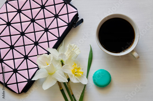 Cosmetic bag, cup of coffee, macaroons and daffodils on white background