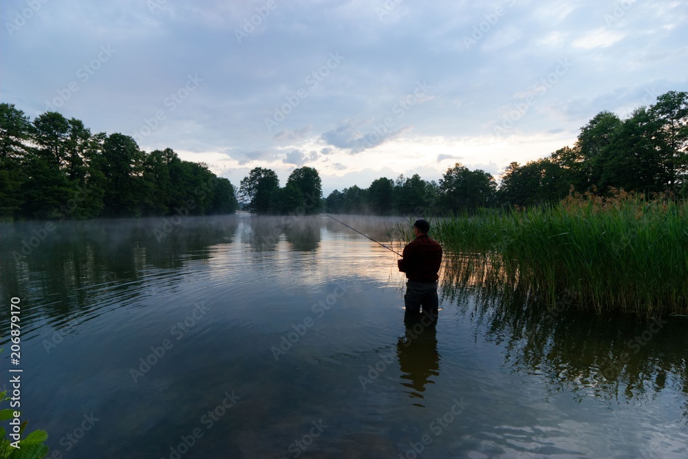 Silhouette of fisherman standing in the lake and catching the fish during sunrise