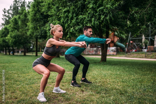 Healthy young man and woman doing squat exercises outdoors.