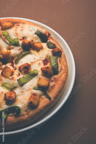 Paneer Pizza is an indian version of Italian dish topped with Cottage Cheese, served in a plate with white sauce. selective focus