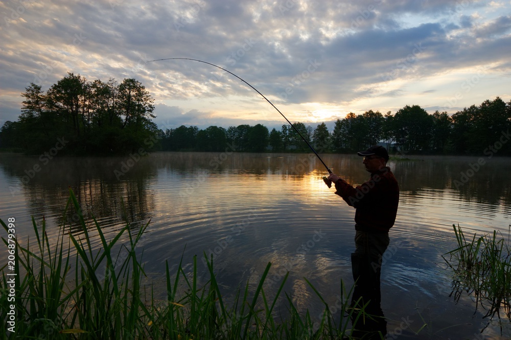 Silhouette of fisherman standing in the lake and catching the fish durring sunrise Silhouette of fisherman standing in the lake and catching the fish durring sunrise