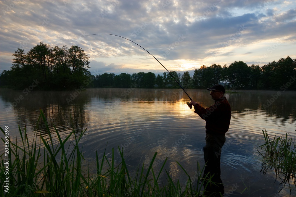 Silhouette of fisherman standing in the lake and catching the fish durring sunrise