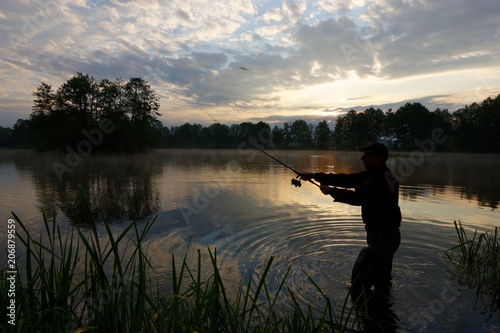 Fisherman throwing fishing bait durring cloudy sunrise