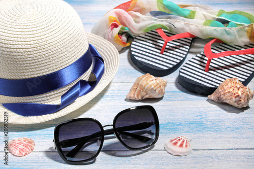 Beach accessories. Black sunglasses and a summer hat with Vietnamese and seashells on a blue wooden background.