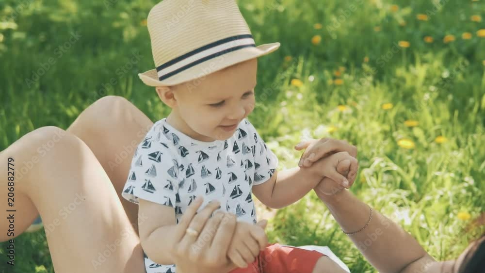 Concept of happy family love. Happy young mother playing on blanket with her cute son under tree at park in slow motion Concept of happy family love. Happy young mother playing on blanket with her cute son under tree at park in slow motion