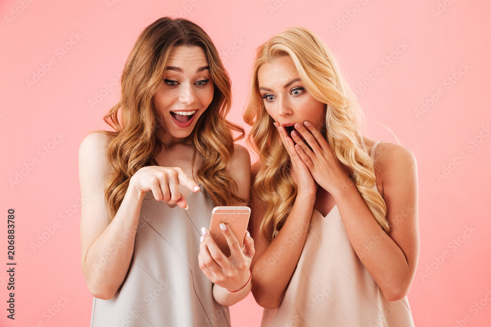 Two surprised pretty women in pajamas using together smartphone Two surprised pretty women in pajamas using together smartphone