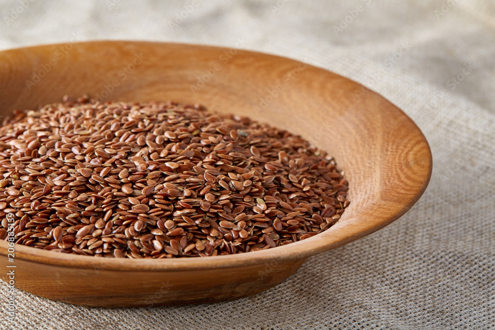 Flax seeds in a wooden plate on homespun tablecloth, top view, close-up. Flax seeds in a wooden plate on homespun tablecloth, top view, close-up.