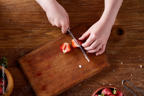 Knife in girl's hand cutting a fresh strawberry on wooden table, top view, selctive focus. photo