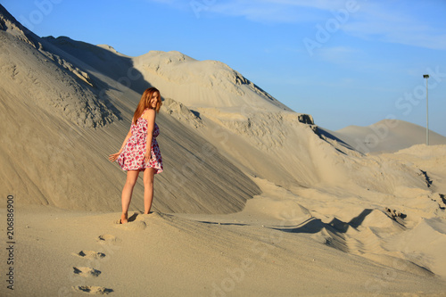 Piękna rudowłosa dziewczyna spaceruje po piaszczystych wydmach.