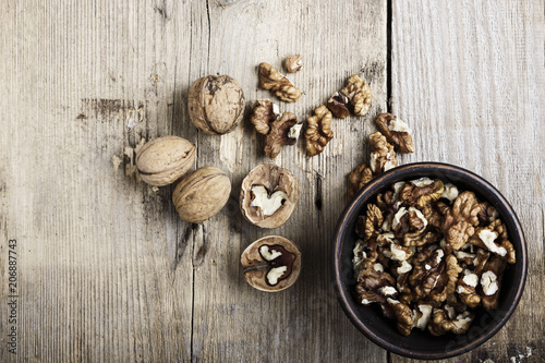 Walnut kernels in a bowl and whole walnuts on table.