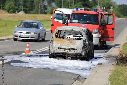 Spalony samochód osobowy na drodze, pożar ugaszony pianą przez straż pożarną.
