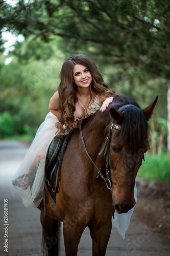 beautiful girl in elegant dress sits on horseback and smiles © Shkriabii