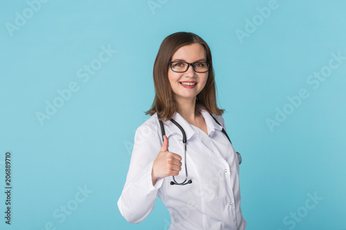 Smiling medical doctor woman with stethoscope showing thumbs up over blue background with copy space