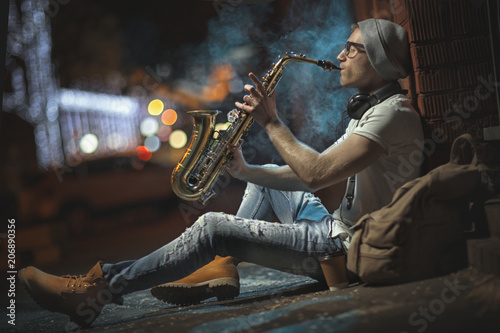 A street musician plays the saxophone in the evening city photo