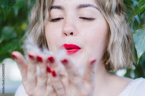 Valokuvatapetti Girl with red lipstick on her lips blowing on poplar fluff on her hands