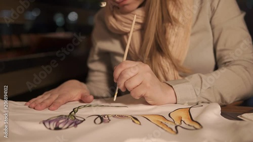 a young woman draws on a swit with watercolor paint and a brush, then she sells it in her workshop for decorating and creating fashionable clothes photo