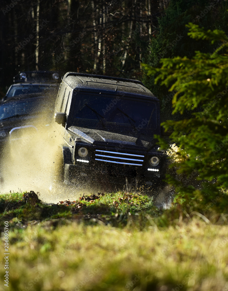 Motor racing in autumn forest. Rallying, competition and four wheel drive concept. Sport utility vehicle or SUV overcomes obstacles. Offroad race on fall nature background Motor racing in autumn forest. Rallying, competition and four wheel drive concept. Sport utility vehicle or SUV overcomes obstacles. Offroad race on fall nature background
