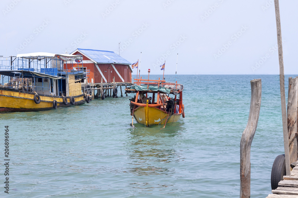 Colorful boat coming to pier of Koh Rong island, Cambodia. Sunny marine travel in tropical island.