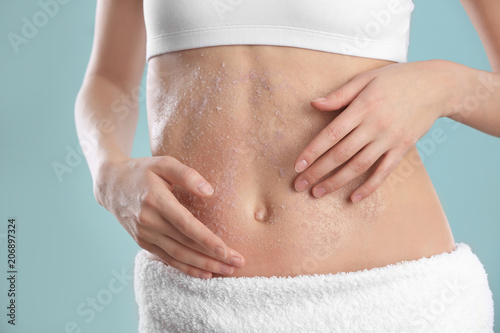 Young woman applying natural scrub on her belly against color background, closeup © New Africa
