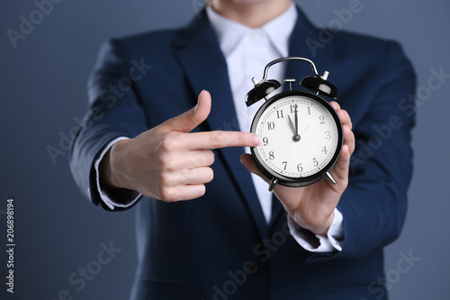 Businesswoman holding alarm clock on color background. Time concept