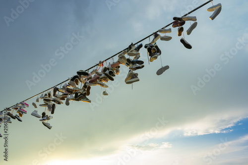 a lot of pairs of shoes hung on a rope for tied shoelaces, against a cloudy sky