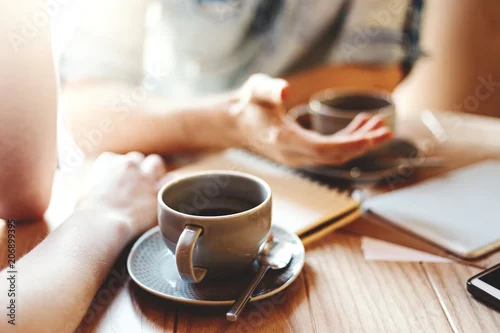 Naklejka na ścianę Przyjaciele opowiada przy kawiarnia stołem podczas kawowej przerwy. Nierozpoznawalni koledzy i koleżanki omawiający problemy biznesowe, skupiają się na filiżance kawy ze spodkiem i łyżeczce do herbaty