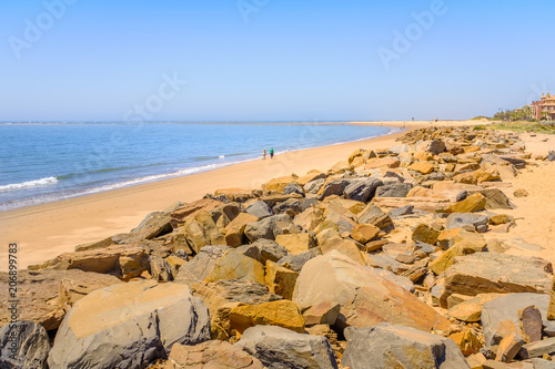 Rocks along the soft sand of the golden beach of Isla Canela beach, Andalucia, Spain on a summer day with blue sky. photo