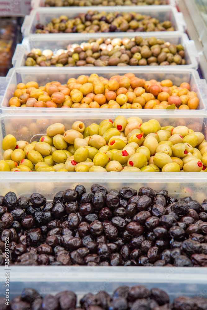 Different kind of green and black olives in brine are sold on the market in containers