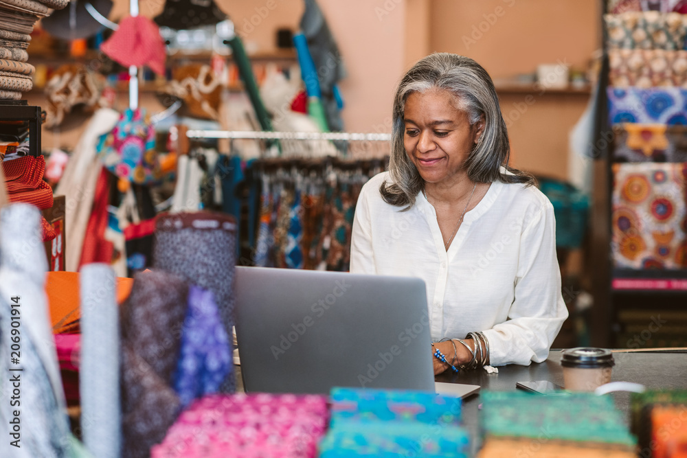 Smiling mature woman using a laptop in her fabric shop