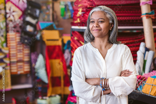 Confident mature woman standing in her colorful fabric shop