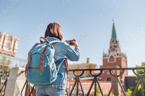Mixed race woman tourist taking pictures on mobile phone on the backgroung the Kremlin wall tower. Travel to Russia concept