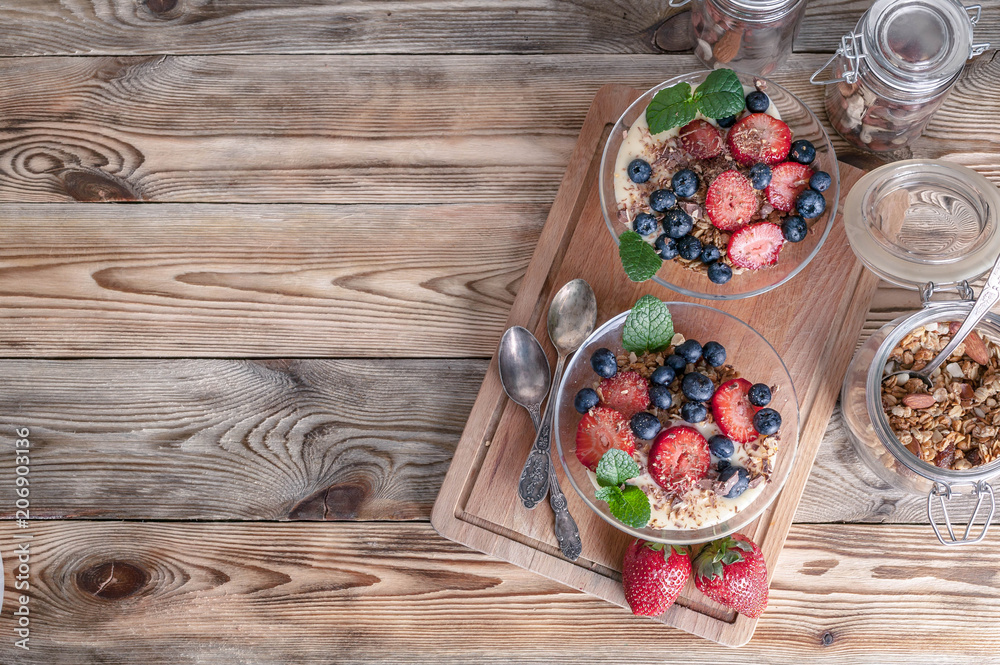 Granola with nuts, yogurt, fresh blueberries and strawberries in a glass bowl on a wooden background. Top view Granola with nuts, yogurt, fresh blueberries and strawberries in a glass bowl on a wooden background. Top view