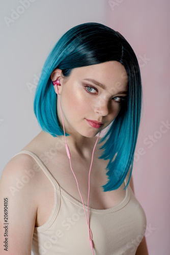 Young beautiful girl with blue hair is using a smartphone with headphones.