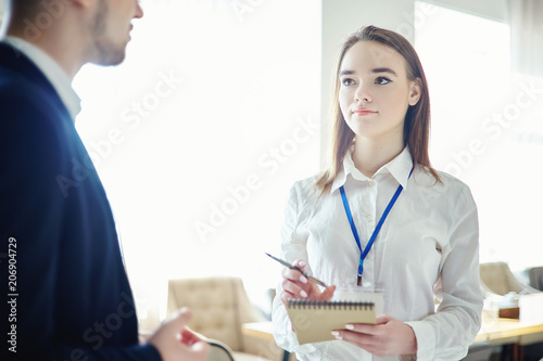 Obraz na plátne Young businesswoman with accreditation badge around her neck talking to unrecognizable male colleague