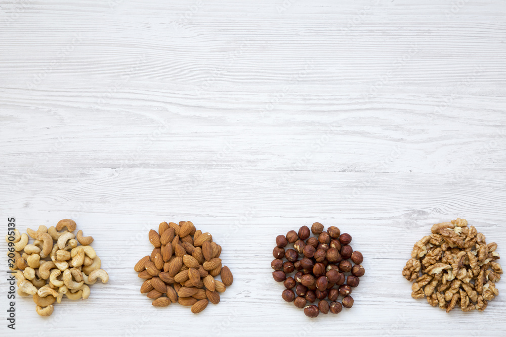 Obraz premium Assortment of nuts on white wooden background. Cashew, hazelnuts, walnuts, almonds. Top view. Copy space and text area.