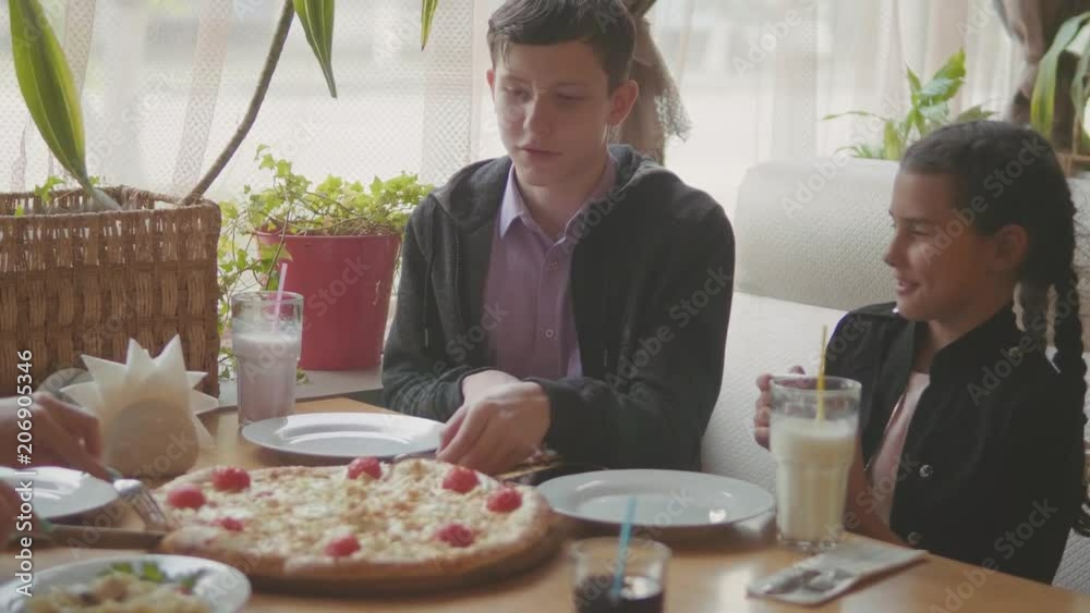 boy teen and girls eats pizza in cafe slow motion video. children eat pizza a delicious pizza. company of people friends eating in lifestyle a cafe. kids eating pizza lifestyle concept boy teen and girls eats pizza in cafe slow motion video. children eat pizza a delicious pizza. company of people friends eating in lifestyle a cafe. kids eating pizza lifestyle concept