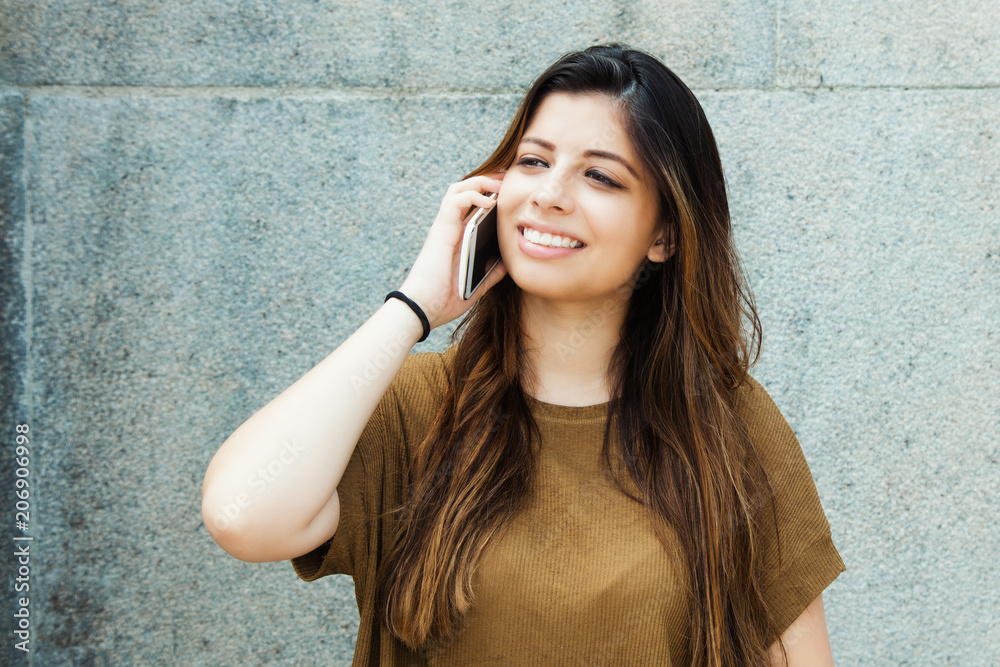 Laughing latin american young adult woman talking on mobile phone