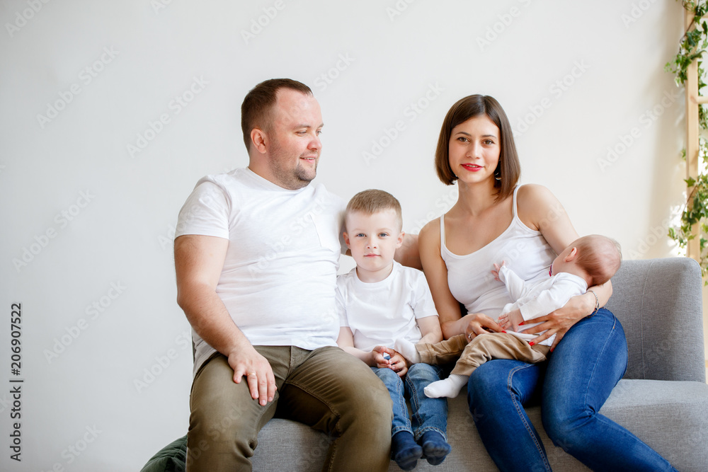 Photo of happy young parents with two small sons sitting on sofa Photo of happy young parents with two small sons sitting on sofa