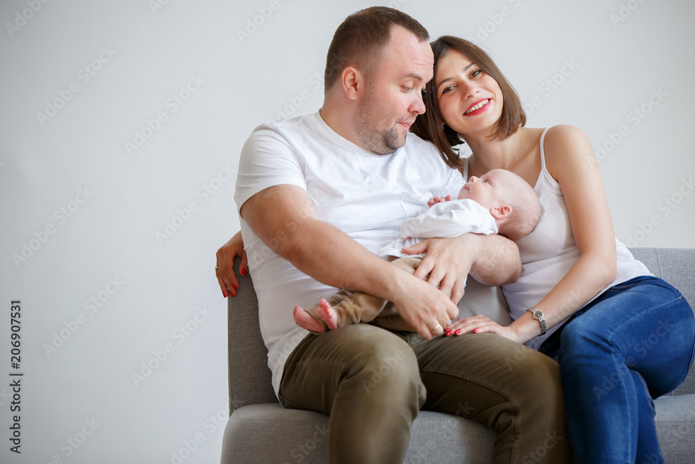 Photo of happy married couple with newborn baby sitting on sofa Photo of happy married couple with newborn baby sitting on sofa