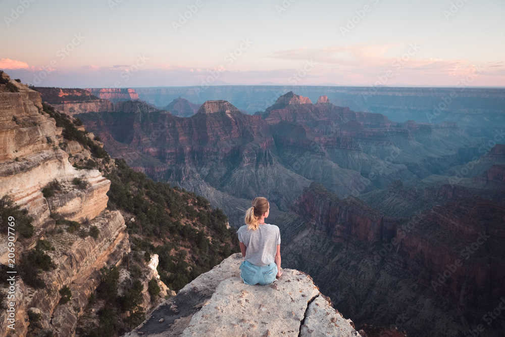 Grand Canyon, USA: Young attractive girl sits on the edge of the cliff, enjoys sunset