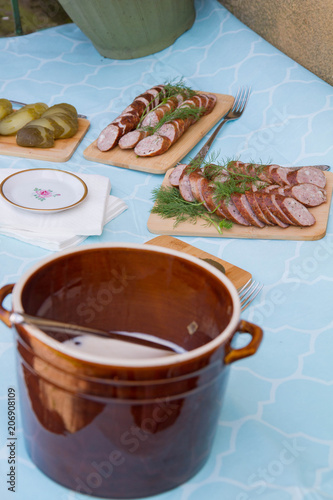 Homemade lard in clay pots, sausage and brined pickles set up on a table at a rustic garden party