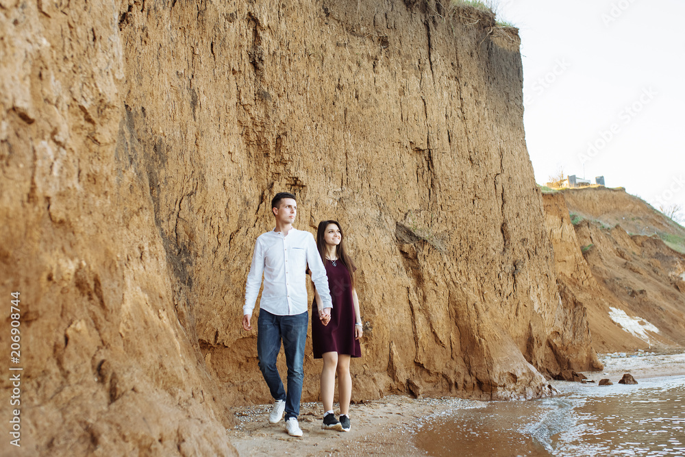 young, happy, loving couple, near the sand wall, on the sea, holding hands go and look at each other, advertising and inserting text