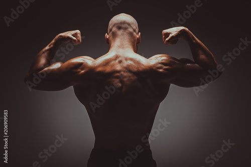 Attractive male bodybuilder flexing his muscles with strong shoulders, biceps, triceps and backin studio shot. Concept Gym Life Style. photo