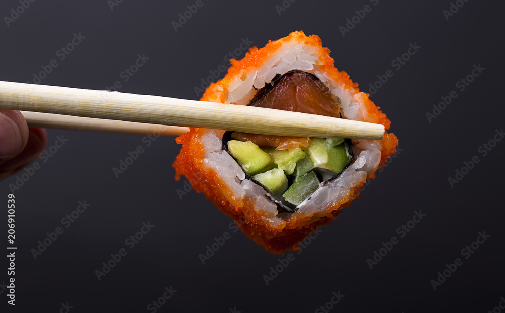 Fingers holding wooden sticks Сalifornia roll with salmon on black background Fingers holding wooden sticks Сalifornia roll with salmon on black background