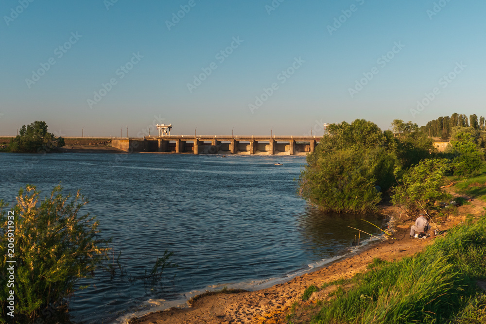 Fisherman on sand coast of river near industrial dum in sunset