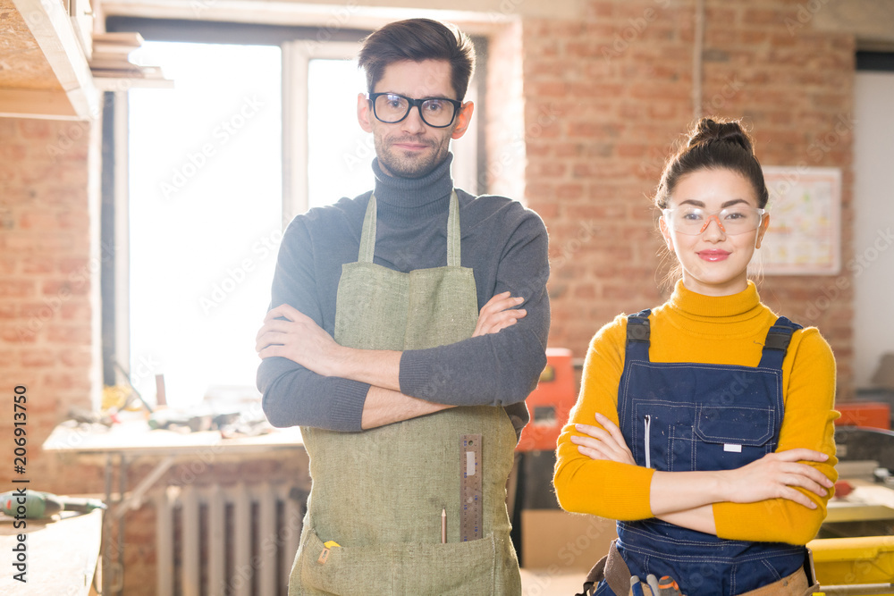 Fototapeta premium Waist up portrait of young female artisan posing in crafting shop standing with arms crossed and looking at camera next to colleague, copy space