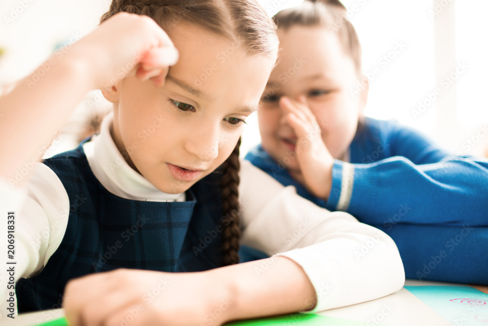Little girl tells the answer to her neighbor at the table at lesson Little girl tells the answer to her neighbor at the table at lesson